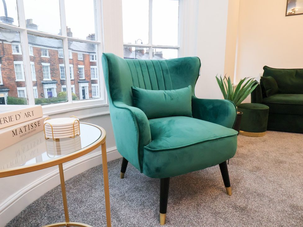 A living room with a green armchair and a side table at Maxwell View in Scarborough