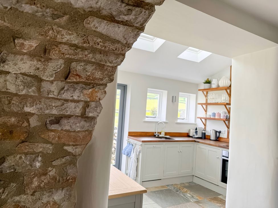 A kitchen with stone wall, sink, and shelves at 7 Litton Slack in Tideswell