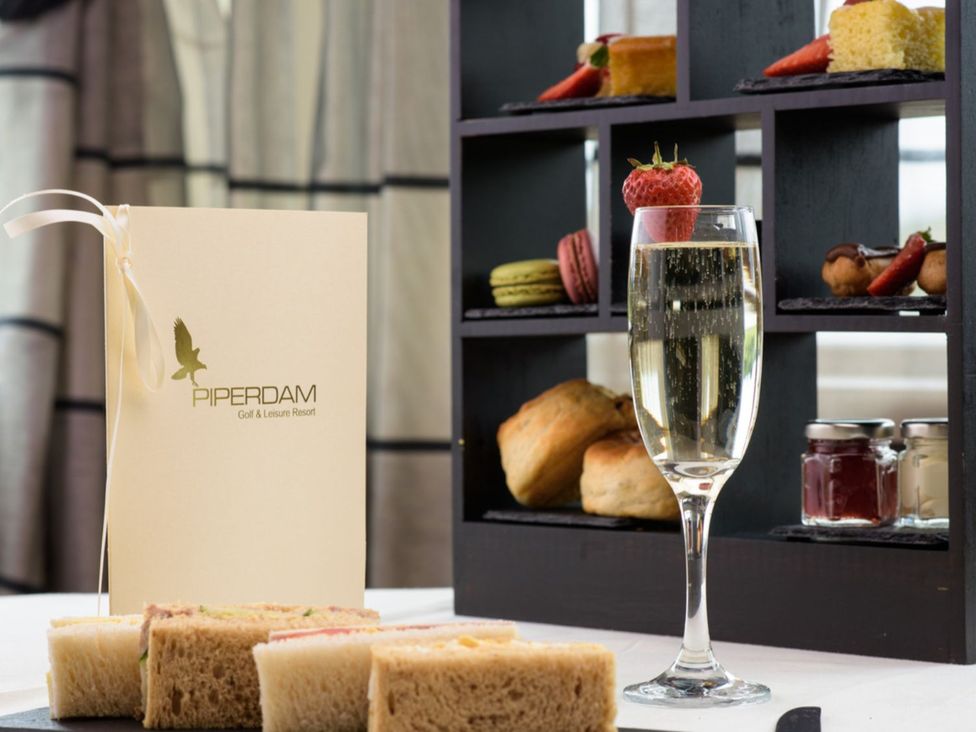 A dining table with sandwiches, champagne, and a menu at Piperdam Golf & Leisure Resort in Dundee