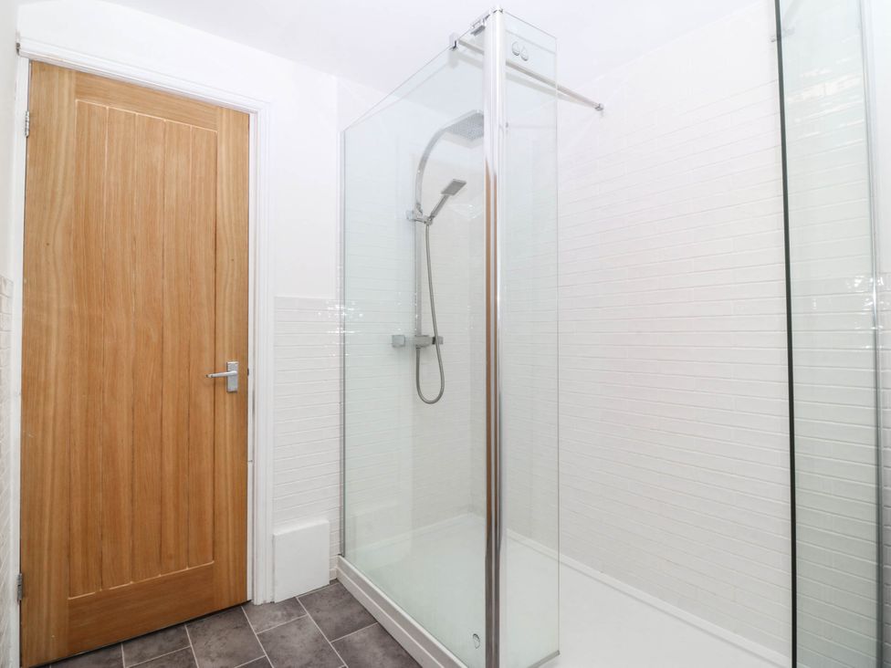 A shower with glass enclosure and wooden door at Mona Lodge in Llandudno