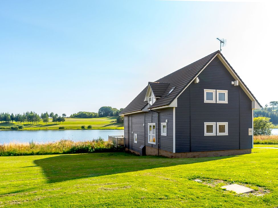 A house near a lake with grass and trees at Lochside Premier Spa in Dundee