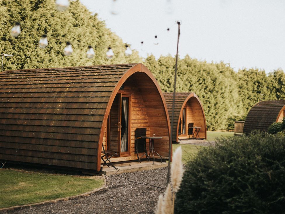 Wooden pods with tables and chairs in a garden at Garden Pod VIP Waltham