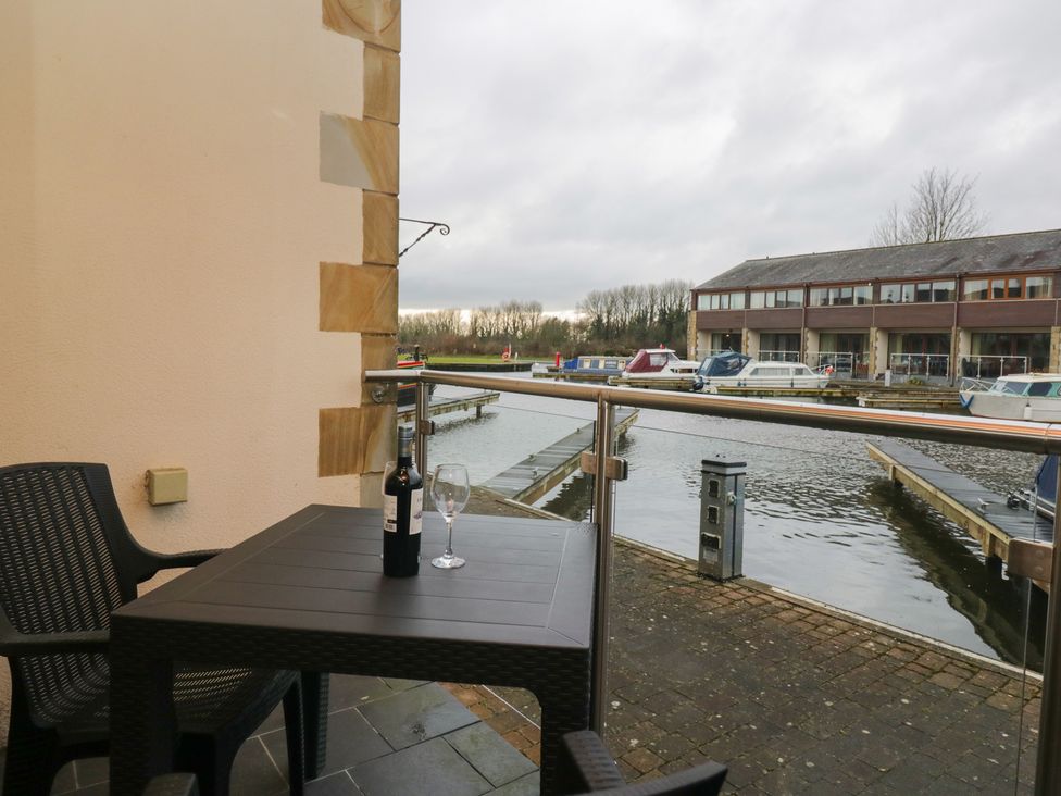 A balcony with a table and wine overlooking the waterway at 6 Swan House in Tewitfield