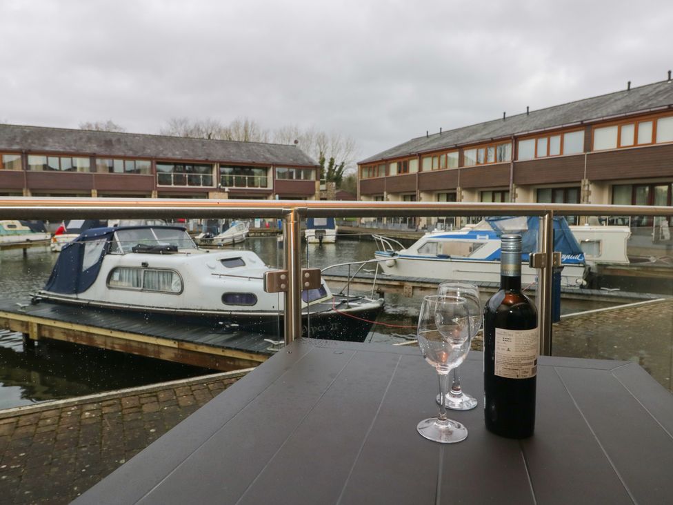 An outdoor area with a wine bottle and glasses overlooking boats at 6 Swan House in Tewitfield