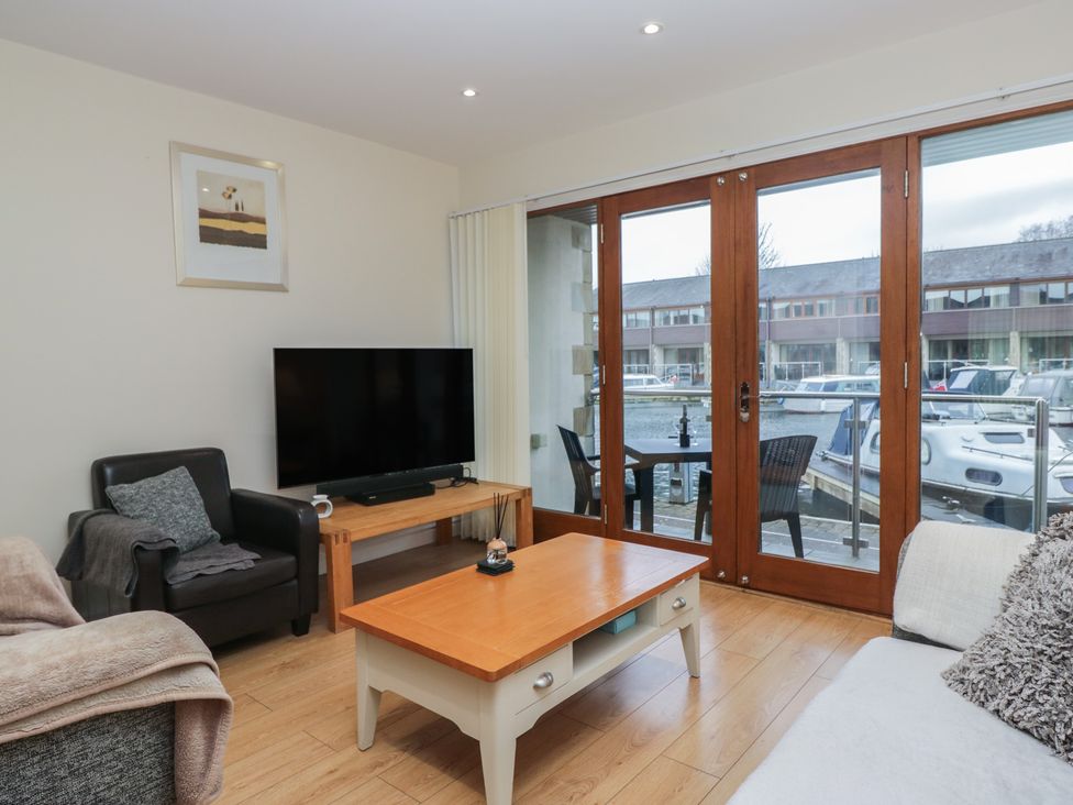 A living room with a television and glass doors opening to a dock at 6 Swan House Tewitfield