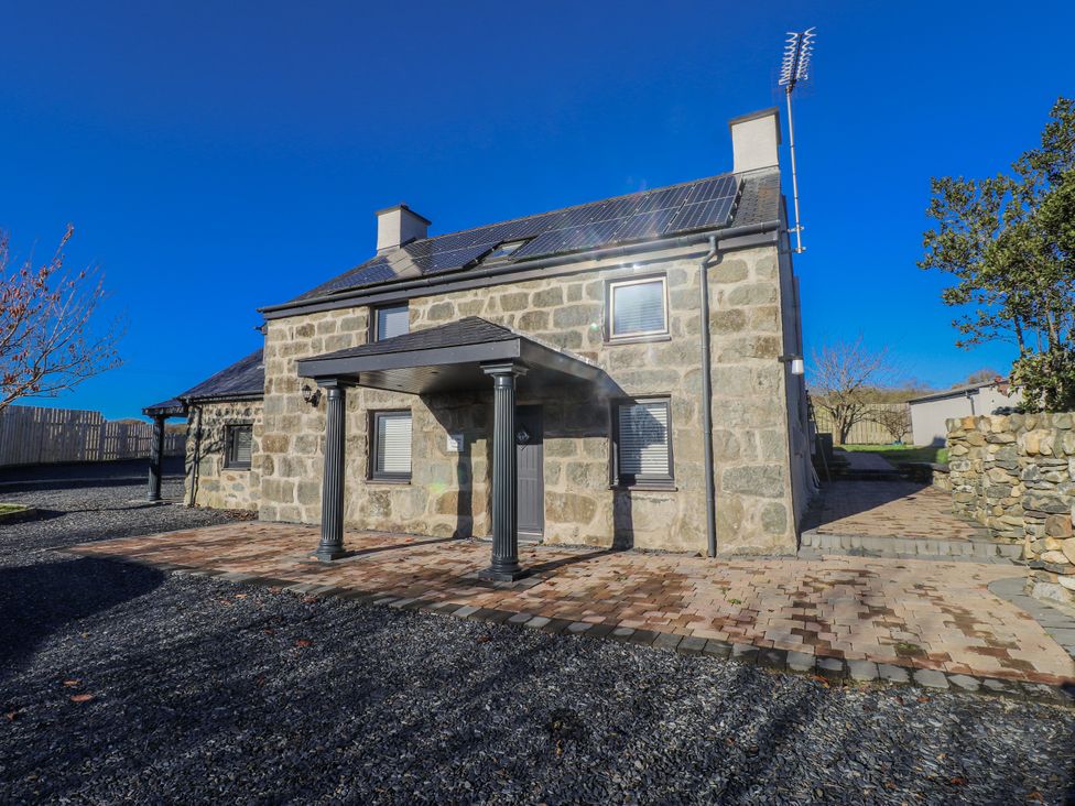 A stone house with a patio and solar panels at Ty'n Lon in Pwllheli
