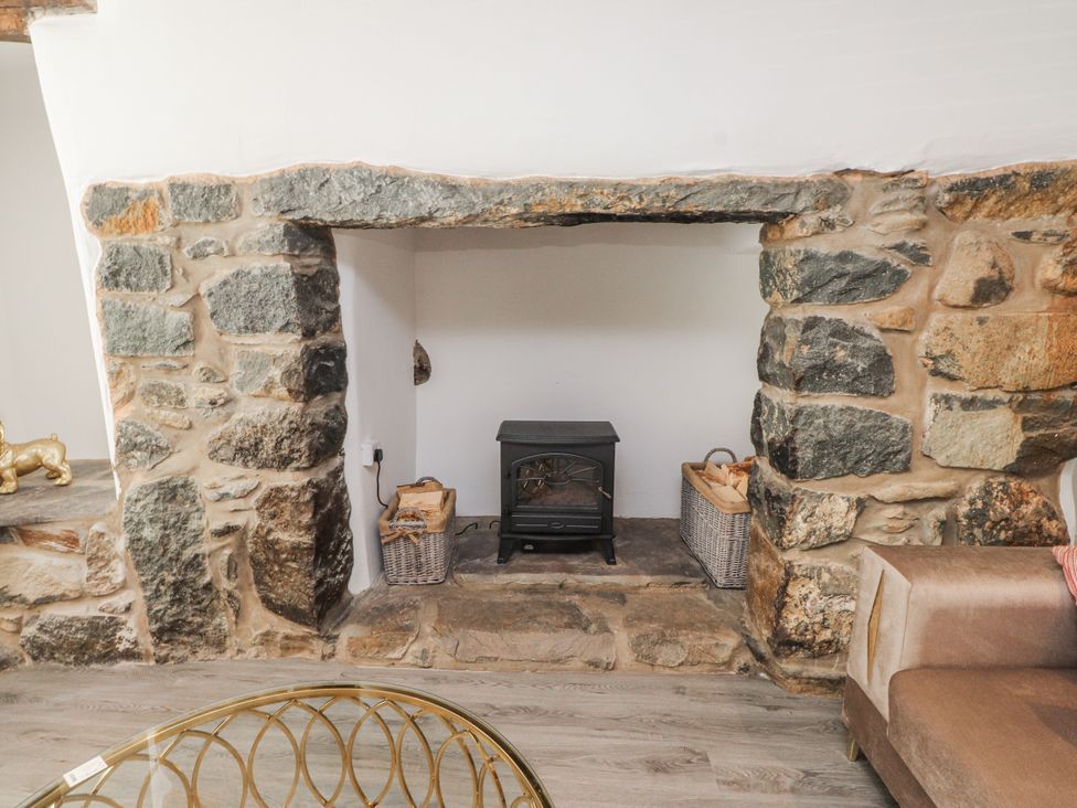 A living room with a stone fireplace and wood stove at Ty'n Lon in Pwllheli