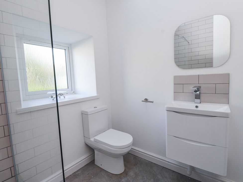 A bathroom with a toilet, sink, and mirror at Ty'n Lon in Pwllheli