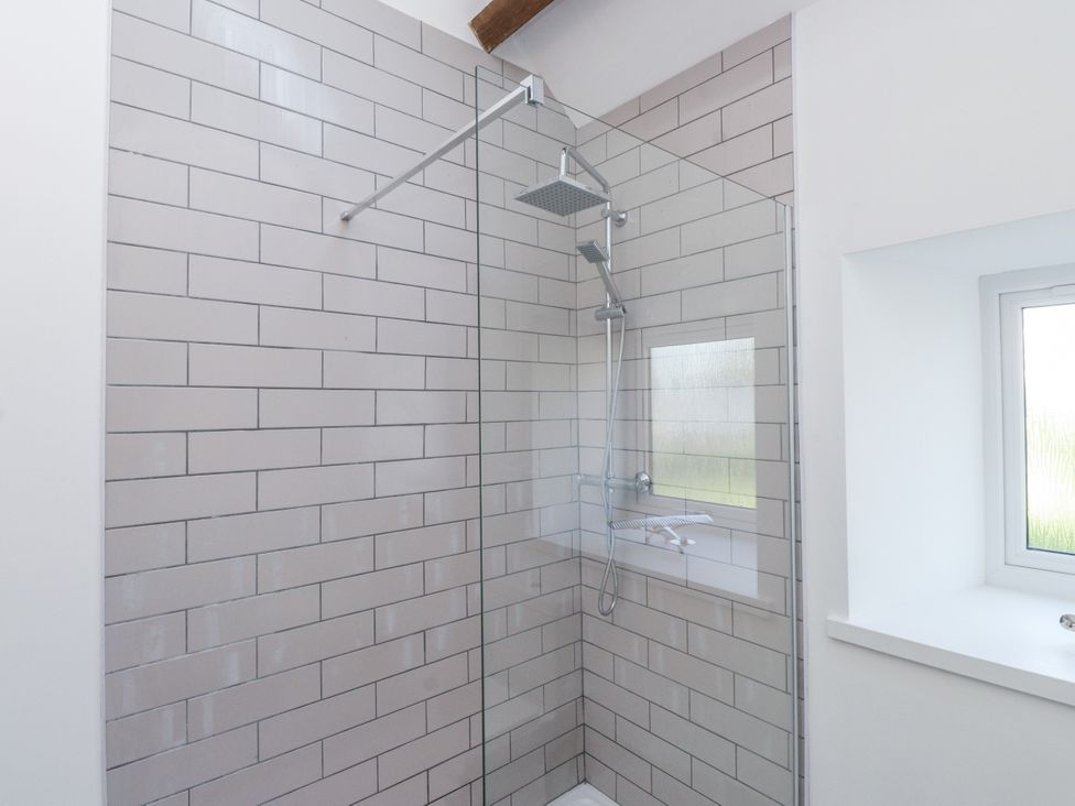A shower with glass panel and tiles at Ty'n Lon in Pwllheli