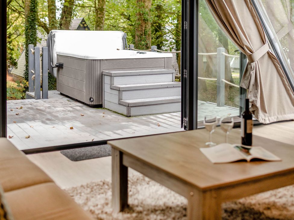 A living room with a hot tub visible through the window at St Ives Lodge 2 Spa in Praze-An-Beeble