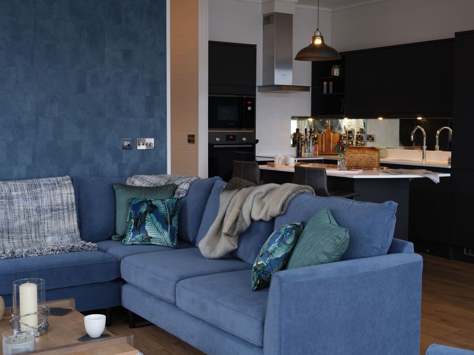 A living room with a blue sofa and kitchen area at Wilde in Laugharne