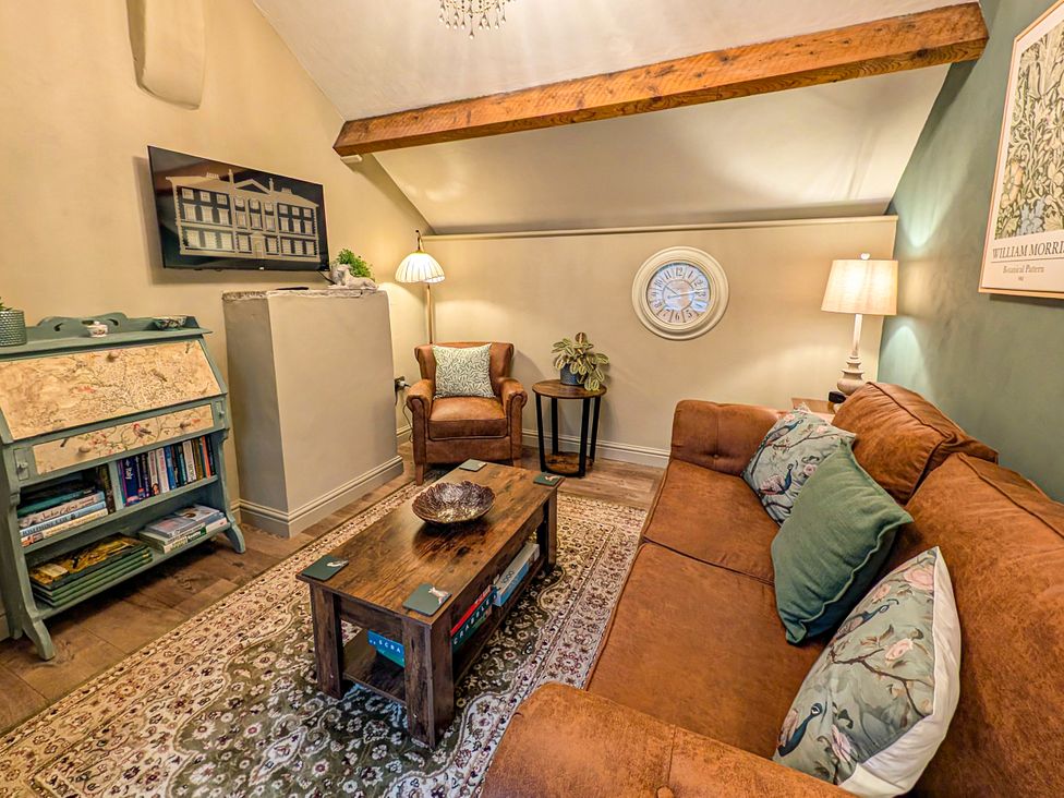 A living room with a sofa, armchairs, coffee table, and television at The Gardeners Cottage in Lytham St. Annes
