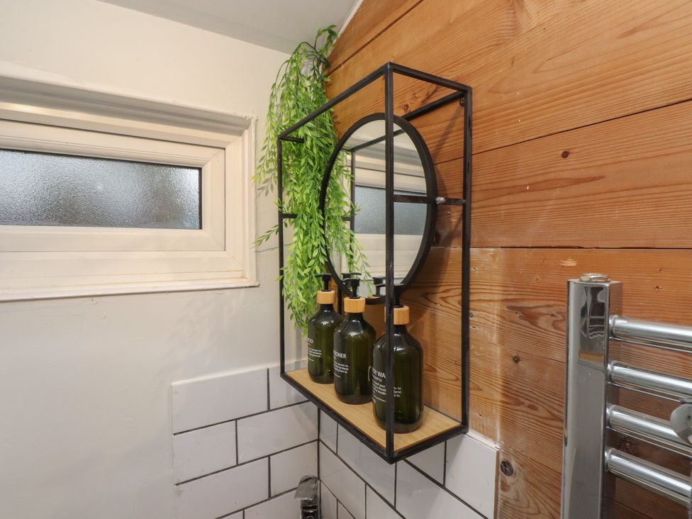A bathroom with a mirror, shelf, bottles, and a window at 20 Chatham Log Cabins, Caernarfon