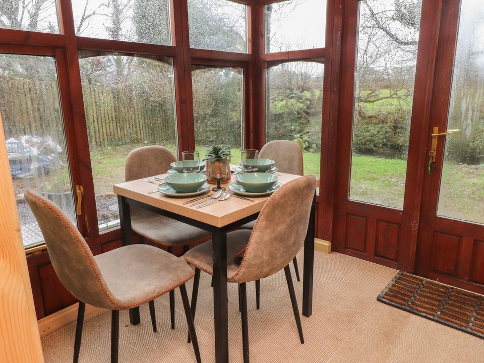 A dining table with chairs and dinnerware in a conservatory at 20 Chatham Log Cabins in Caernarfon