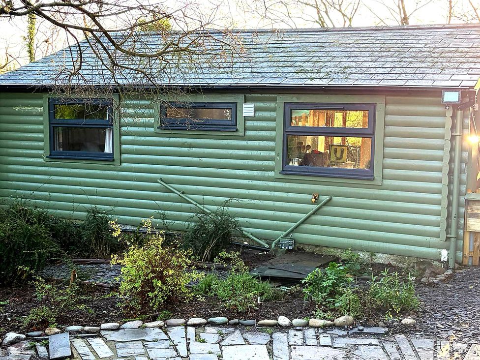 An exterior view of a green log cabin with windows at 20 Chatham Log Cabins in Caernarfon