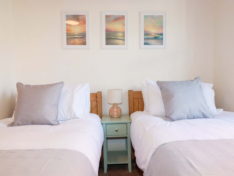 A bedroom with two beds and framed pictures at Chapel Cottage in Mevagissey