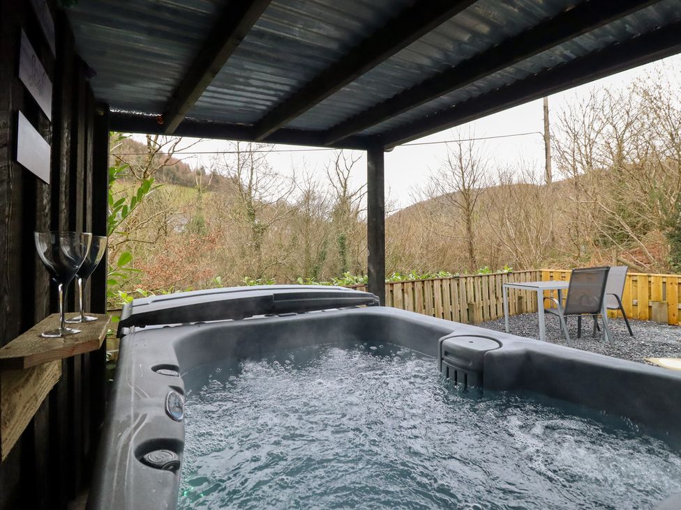 A hot tub with glasses and a table in an outdoor area at Lodge at Nadur Commins Coch near Machynlleth