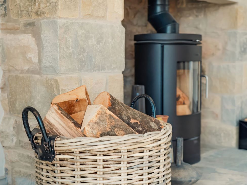A living room with firewood in a basket and a wood stove at The Old Watermill Beadnell
