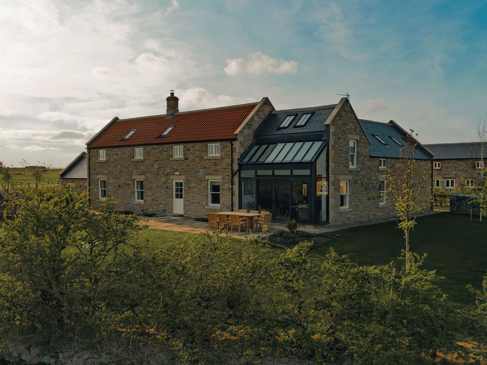 An exterior view of a house with a garden and seating area at Mill Farm House Beadnell