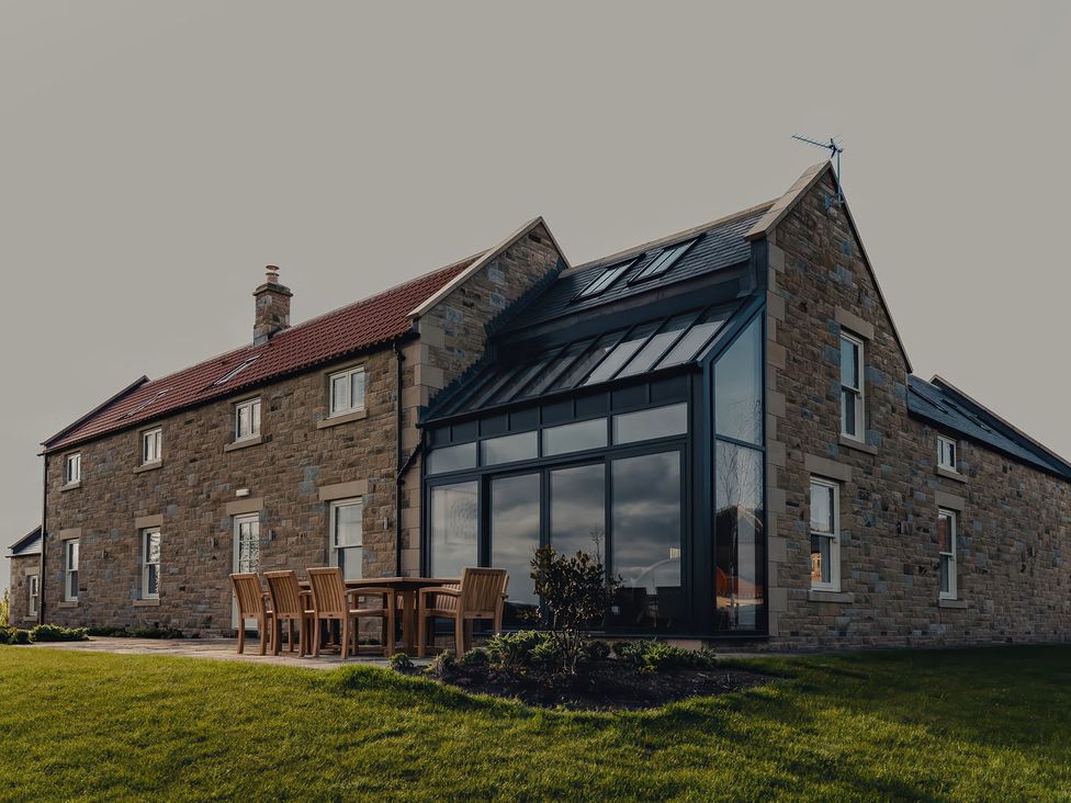 A house with large windows and outdoor seating at Mill Farm House Beadnell