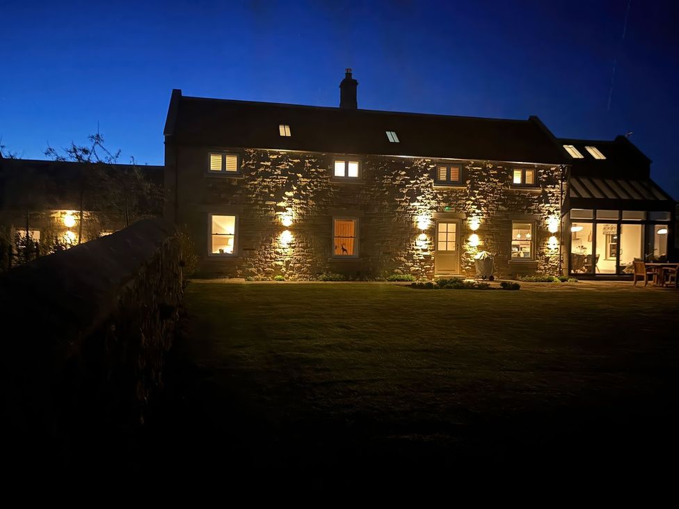 A house with illuminated windows and garden at Mill Farm House Beadnell
