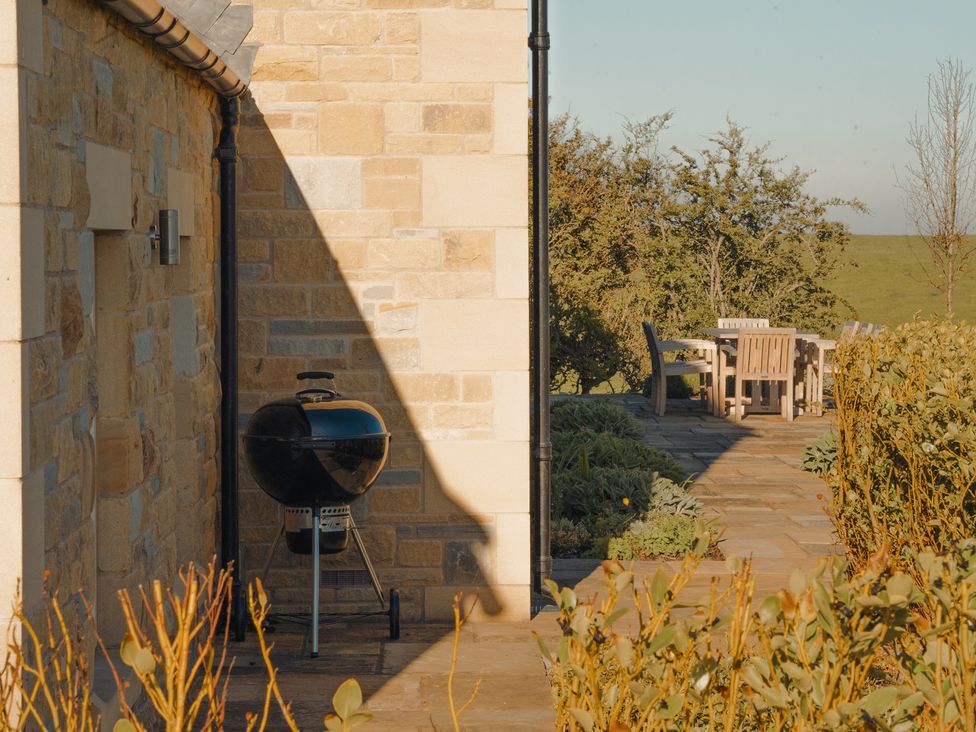 An outdoor area with a grill beside a stone wall at Mill Farm House Beadnell