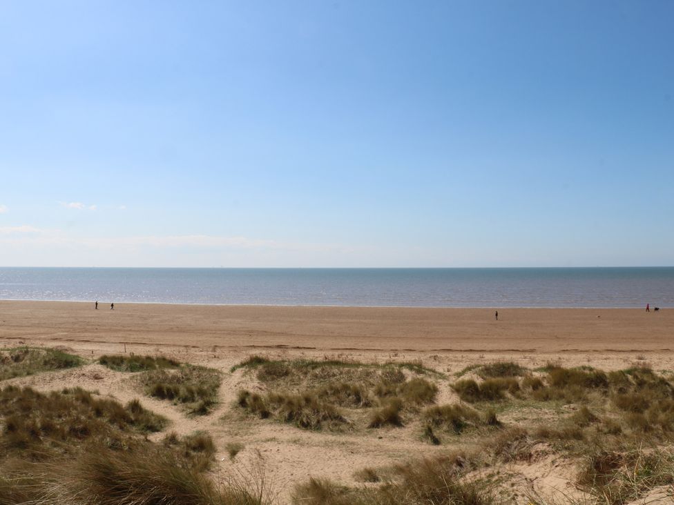 A beach scene with sand, sea and people at the shoreline in the area