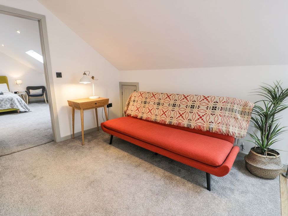 A snug with a sofa, table, lamp, and plant at Cae Sam in Pentraeth