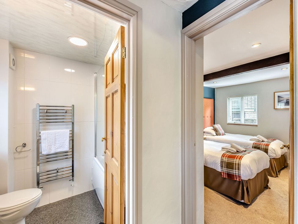 A bathroom with a toilet and towel rail leading to a bedroom with two beds at Caldew Cottage Spa in Penrith