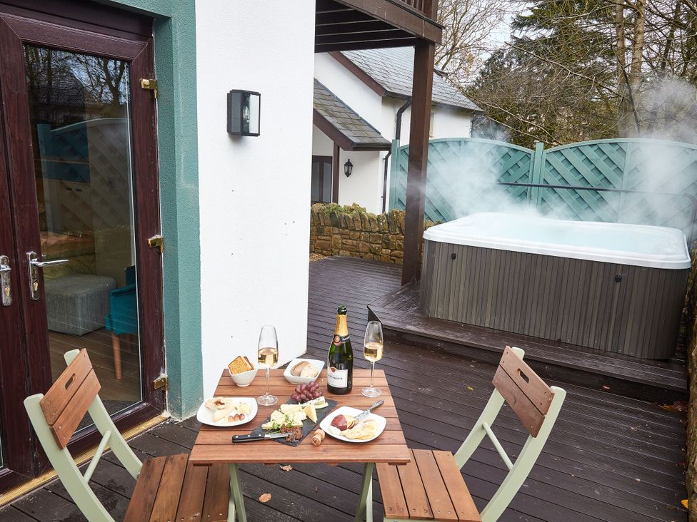 An outdoor area with a hot tub and dining setup at Troutbeck Cottage Spa in Penrith