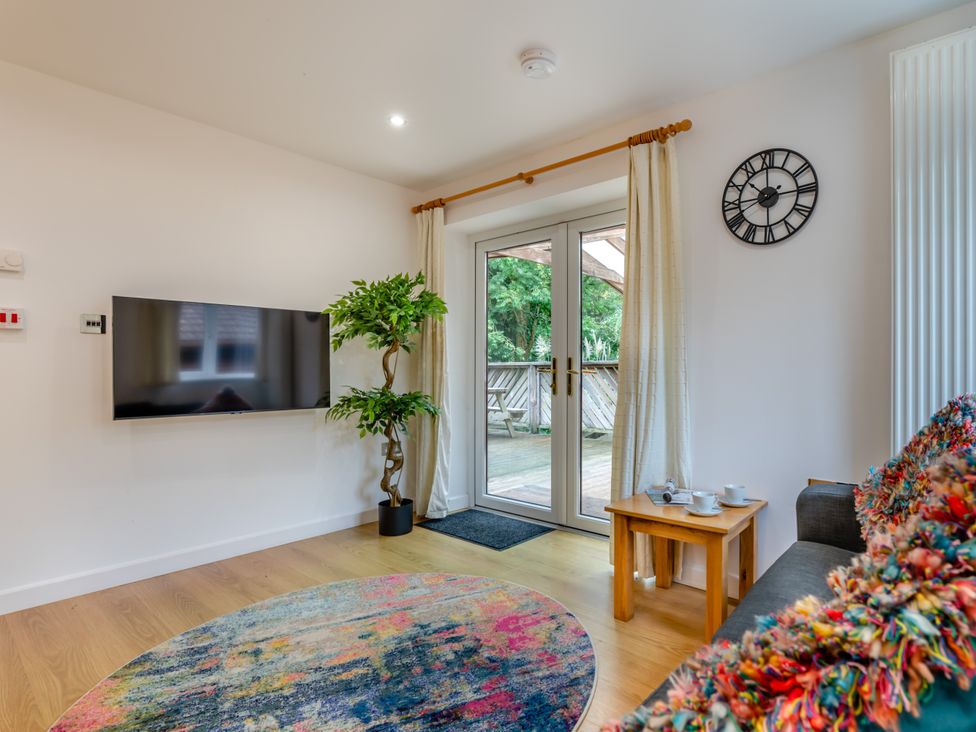 A living room with a television and doors leading to a deck at Poldark Spa Pet Perranporth