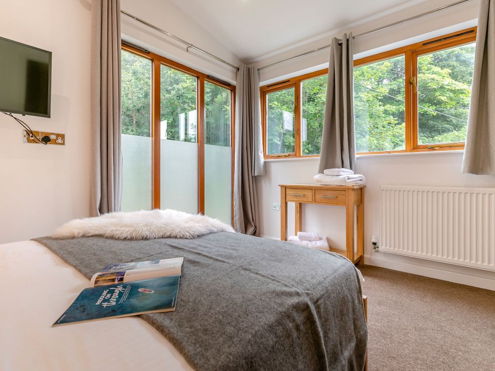 A bedroom with a bed and windows at Treehouse Spa in Perranporth