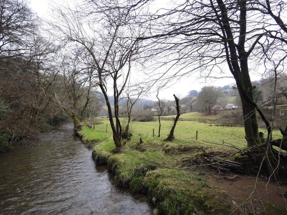 A view of a river bordered by trees and a grassy field at Nethercote Byre Minehead