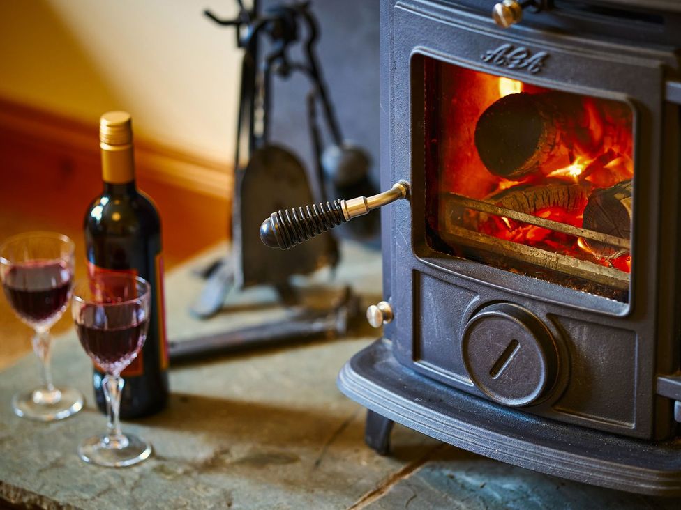 A wood stove with logs burning and wine glasses at Hazel Lodge in Blairgowrie