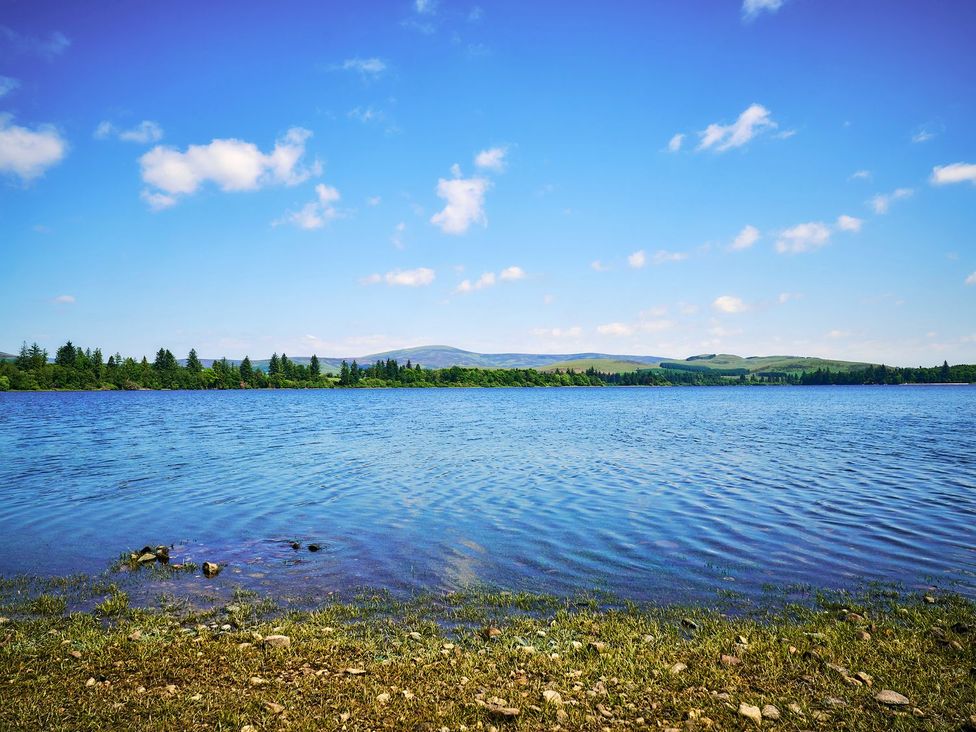 A lake with trees and mountains in the background at West Lodge in Kirriemuir