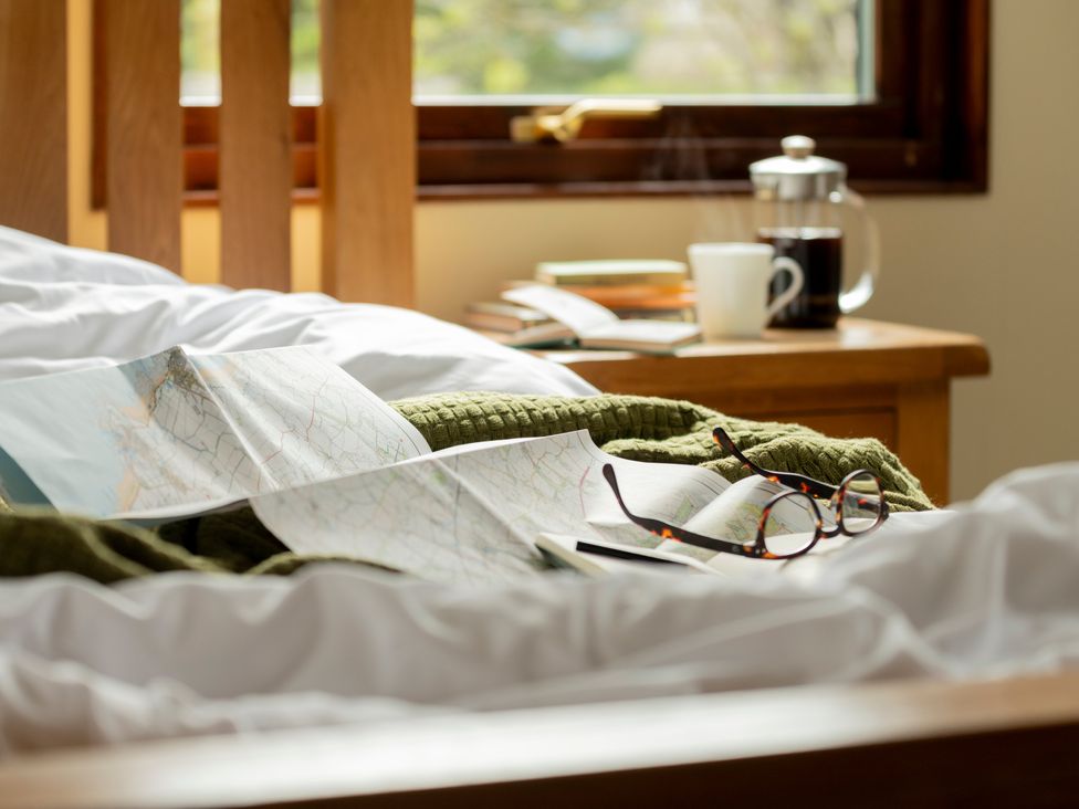 A bed with a map, book, coffee cup, and glasses at The Derwent in Slaley