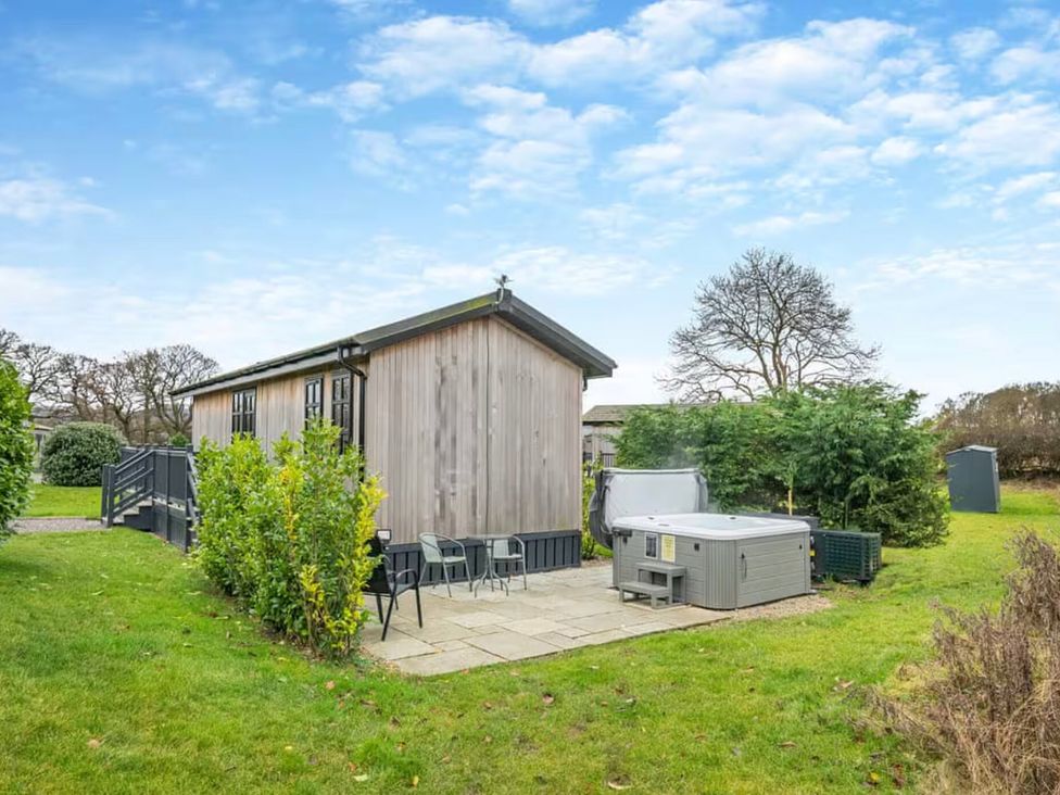 An outdoor area with a wooden cabin, table, chairs, and a hot tub at Stokesley (Pet) Great Ayton