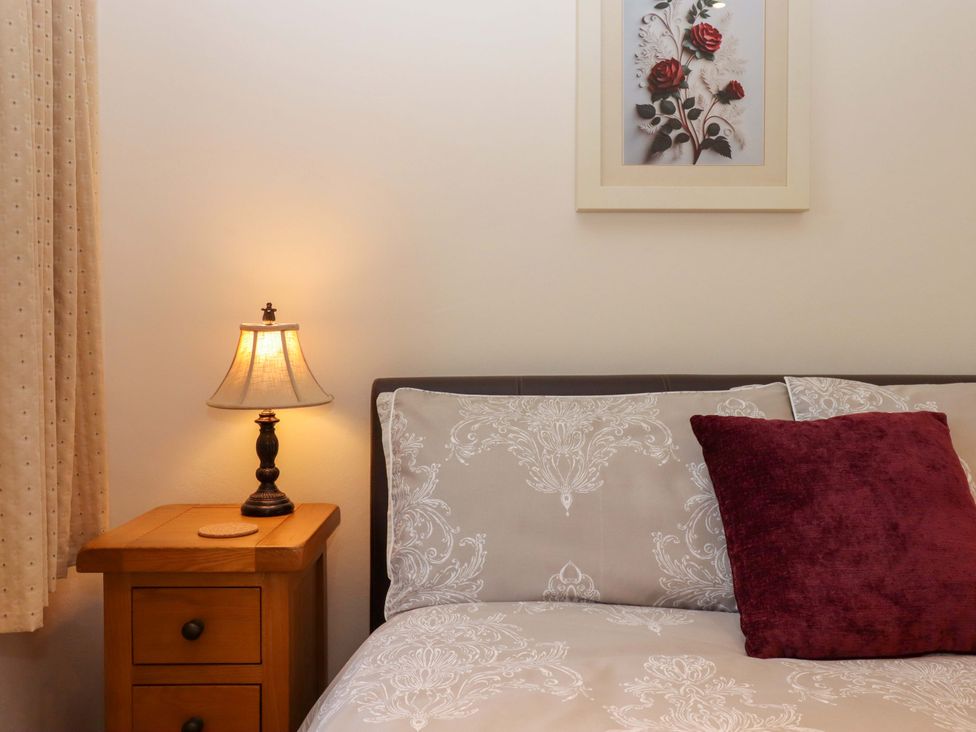 A bedroom with a bed, bedside table, lamp, and picture at Grange Cottage in Coldridge