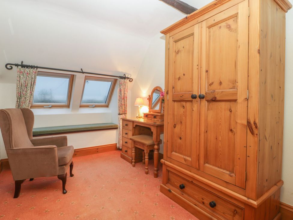 A bedroom with a wardrobe, armchair, and vanity table at The Stables in Sturminster Newton