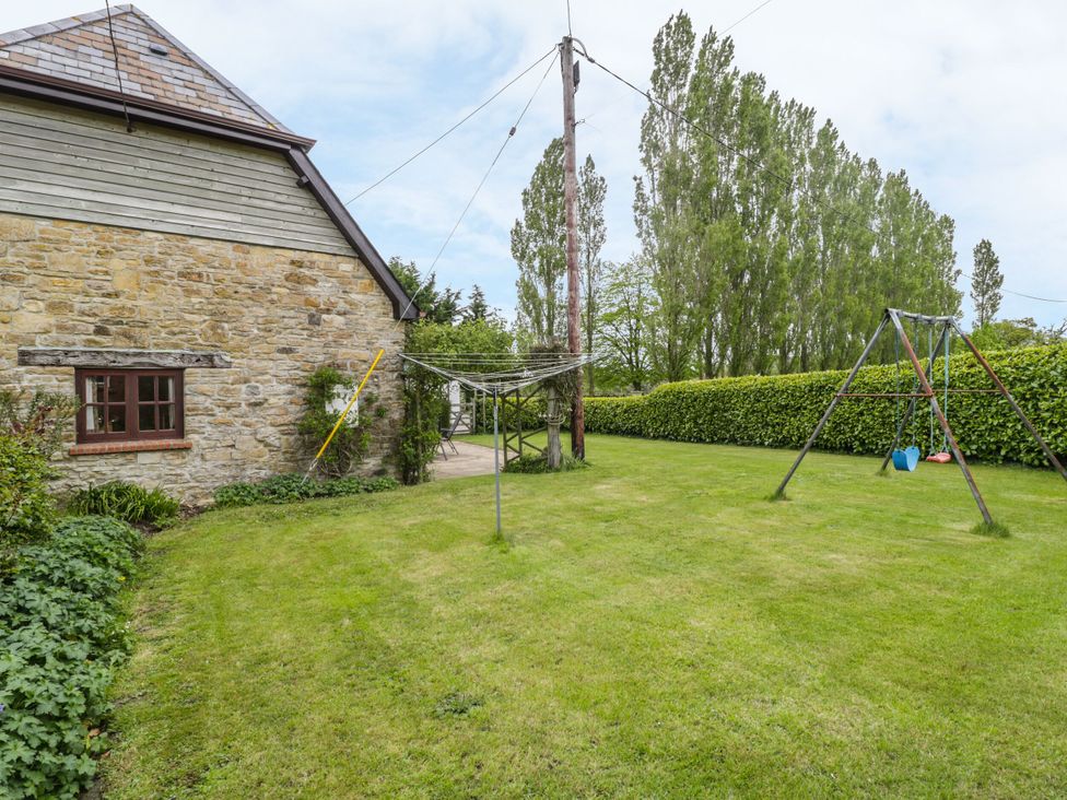 A garden with a stone wall and swingset at The Stables in Sturminster Newton