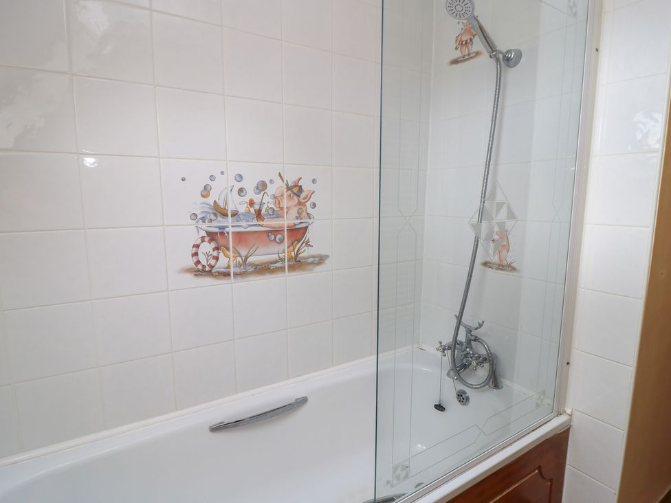 A bathtub with a shower and decorative tiles at The Stables in Fifehead Neville near Hazelbury Bryan