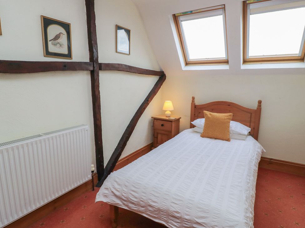 A bedroom with a bed, nightstand, and windows at The Stables in Fifehead Neville near Hazelbury Bryan