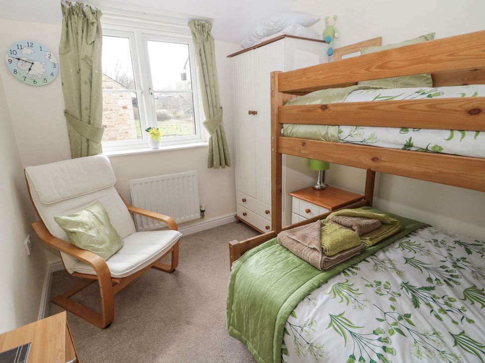 A bedroom with a bunk bed and armchair at Ramblers Cottage in Alnwick
