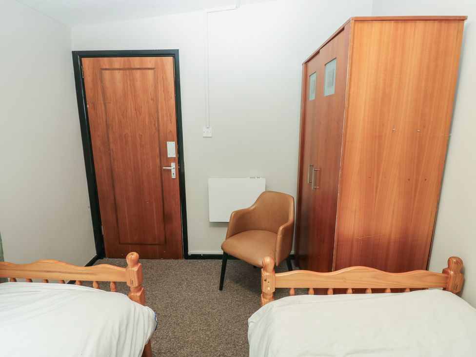 A bedroom with two beds, a wardrobe, a chair, and a door at Cabin No. 15 - Salt and Fern Cabins near Goytre near Port Talbot