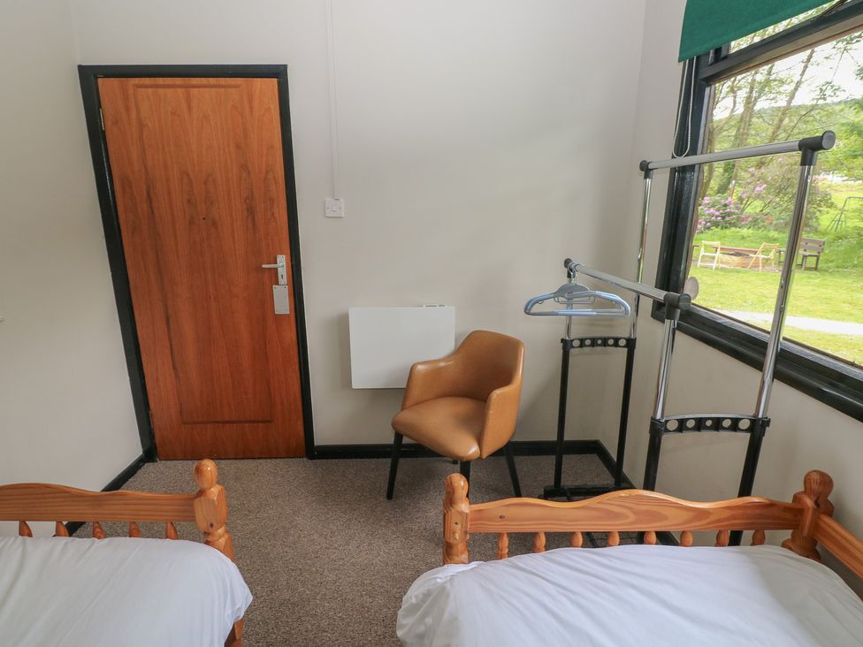 A bedroom with two beds, a chair, and a clothes rack at Cabin No. 15 - Salt and Fern Cabins Goytre near Port Talbot