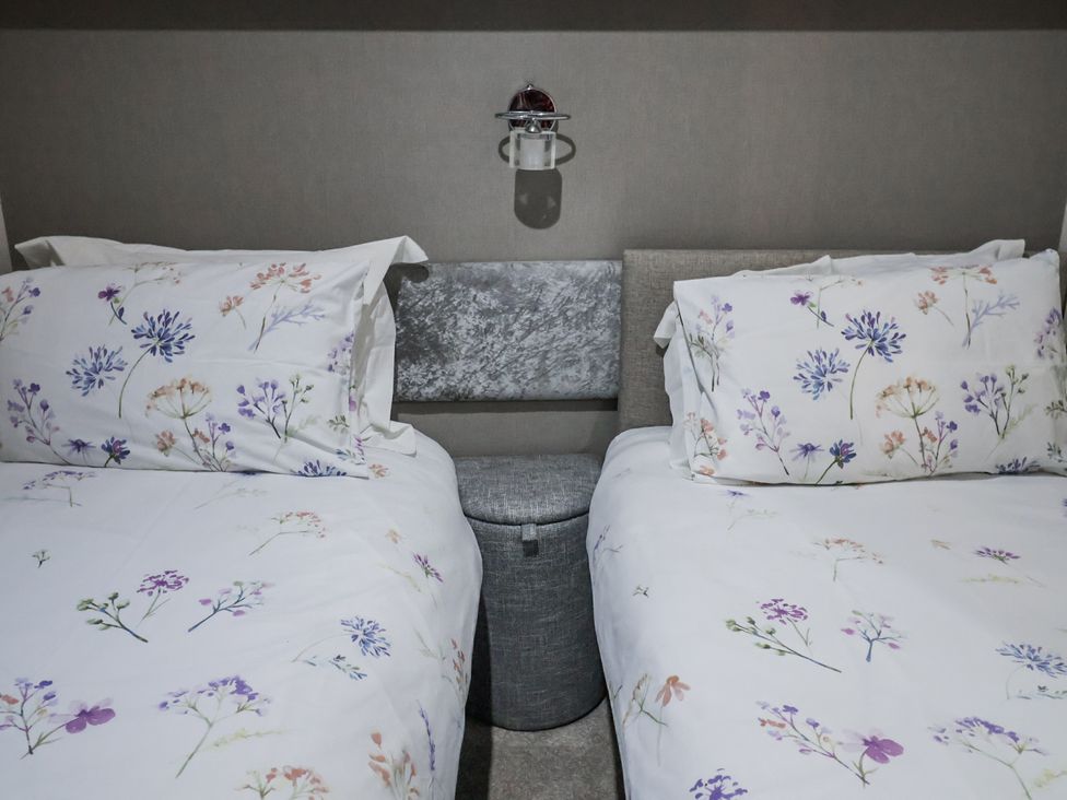 A bedroom with two beds and a bedside table at Lakeside Lodge in Stonham Aspal