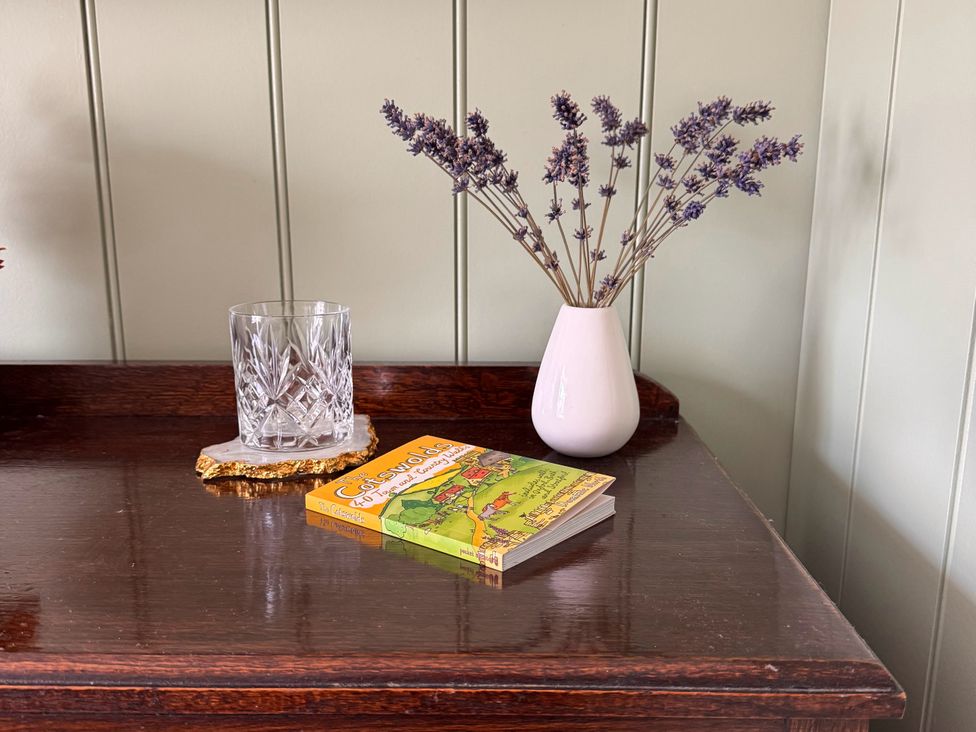 A table with a glass, vase with lavender, and a book at Cotswolds Farmhouse Cottage