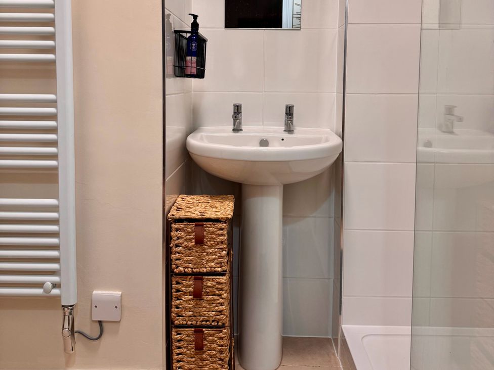 A bathroom with a sink, faucet, towel radiator, and storage baskets at Cotswolds Farmhouse Cottage