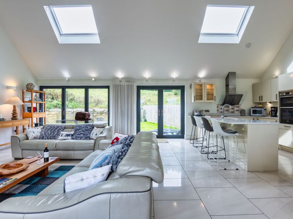 A living room with a sofa and kitchen island at Beachcombers in Marhamchurch
