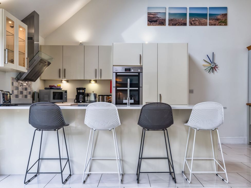 A kitchen with a sink and stools at Beachcombers in Marhamchurch